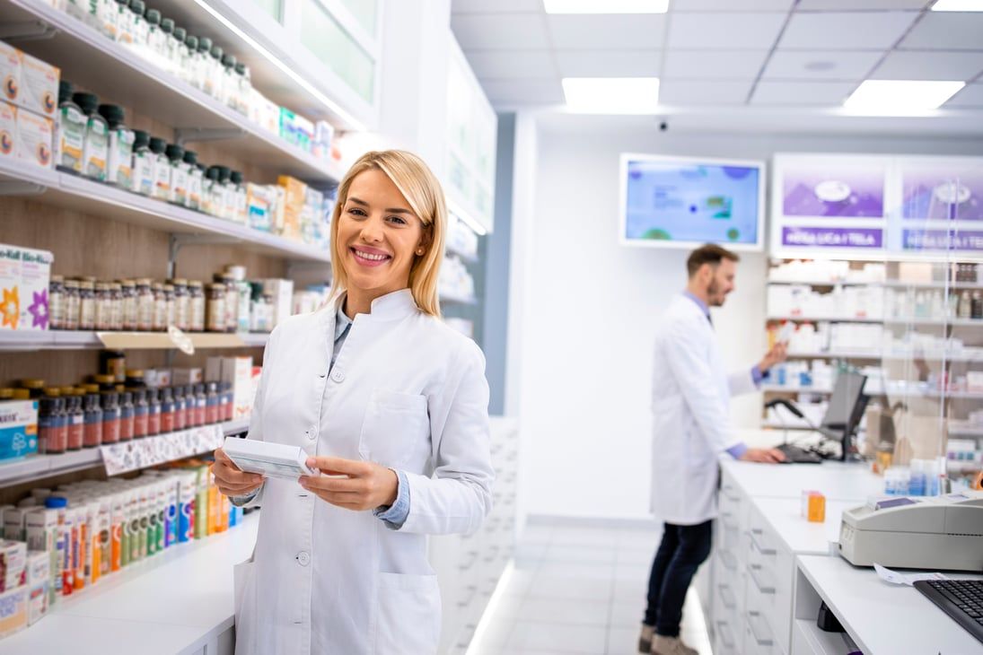Pharmacienne souriante dans son officine, au milieu des rayons