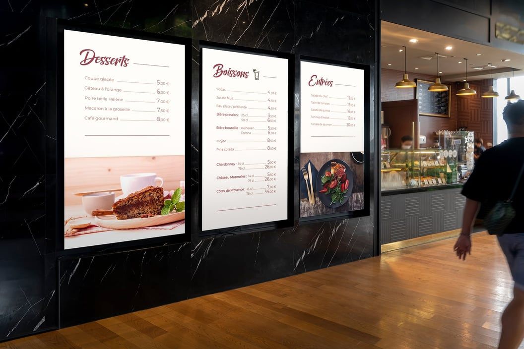Three digital menu screens mounted on a wall above the counter of a fast-food restaurant