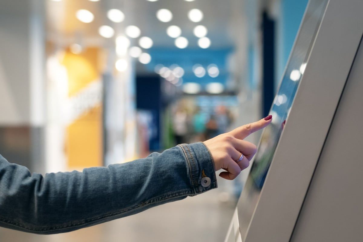 Une main pointe l'écran tactile d'une borne Touchify dans un centre commercial.